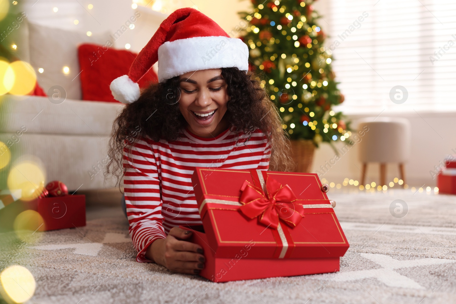 Photo of Happy young woman in Santa hat with Christmas gift at home