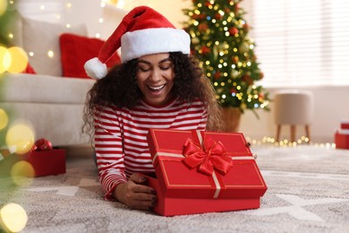 Photo of Happy young woman in Santa hat with Christmas gift at home