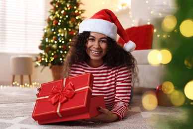 Photo of Happy young woman in Santa hat with Christmas gift at home