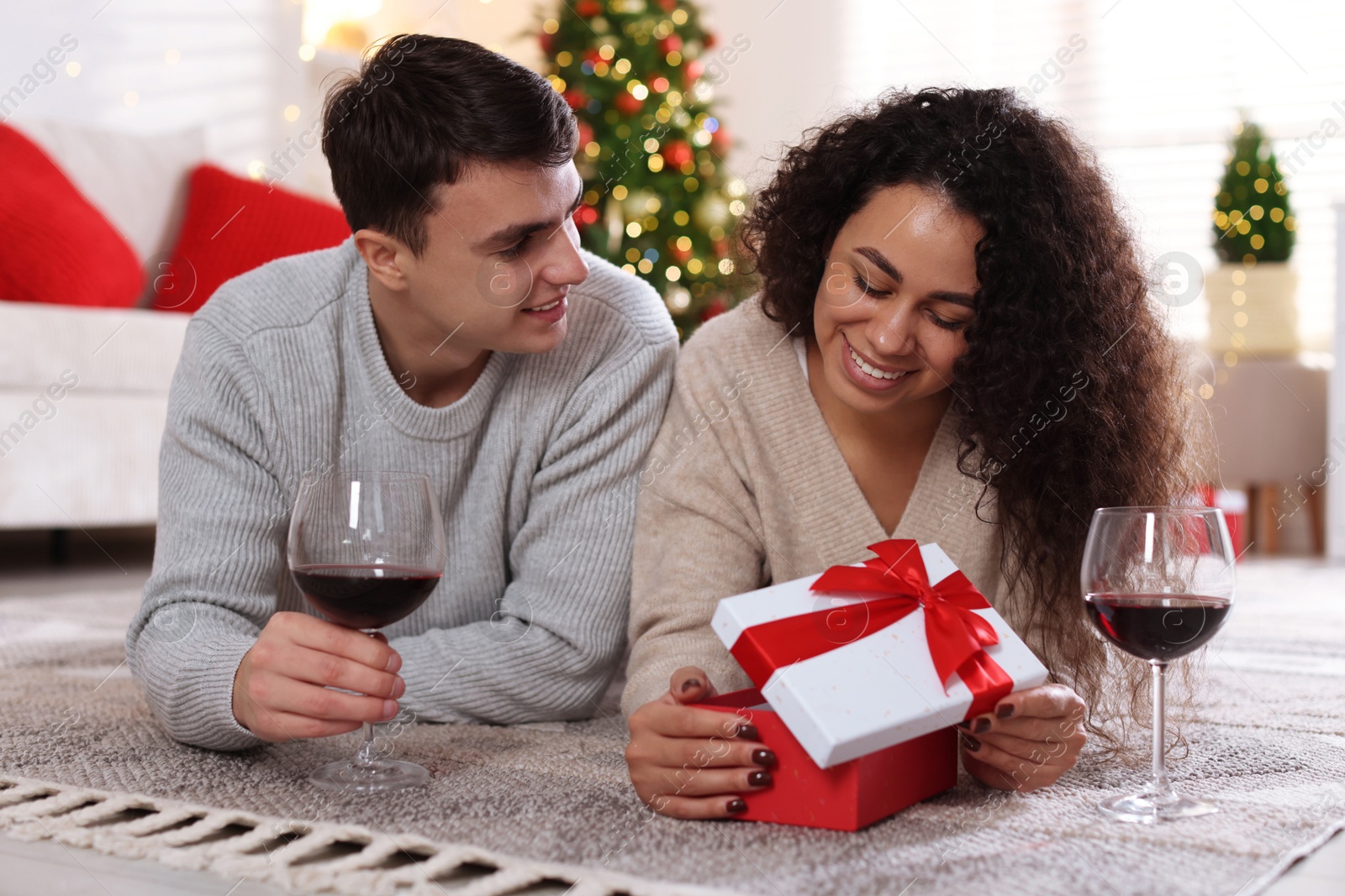 Photo of Happy couple with Christmas gift and glasses of wine spending time together at home