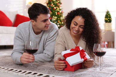 Photo of Happy couple with Christmas gift and glasses of wine spending time together at home