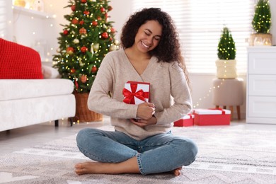 Photo of Happy young woman with Christmas gift at home