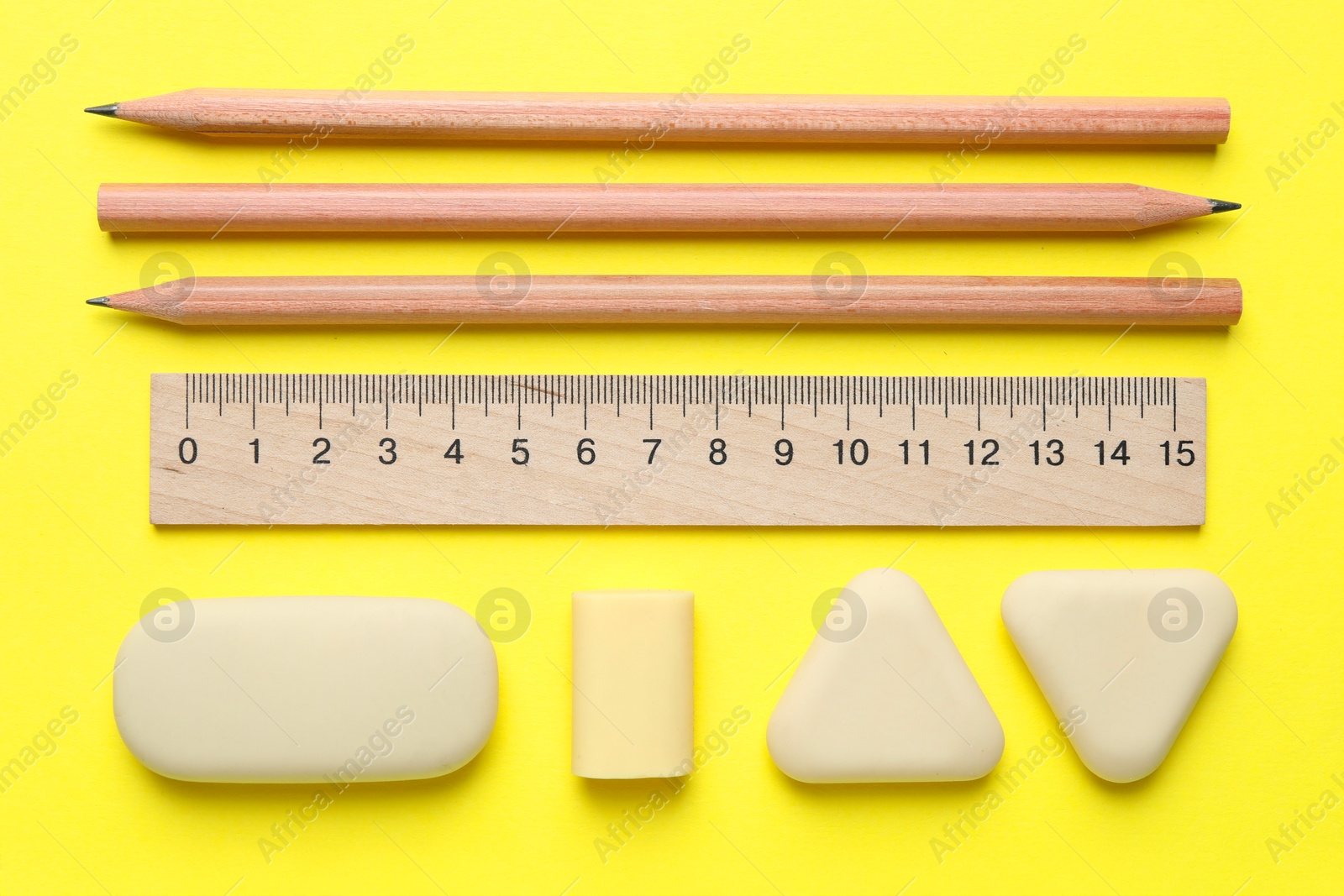 Photo of Erasers and other stationery on yellow background, flat lay