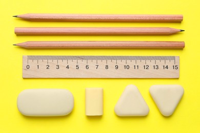 Photo of Erasers and other stationery on yellow background, flat lay