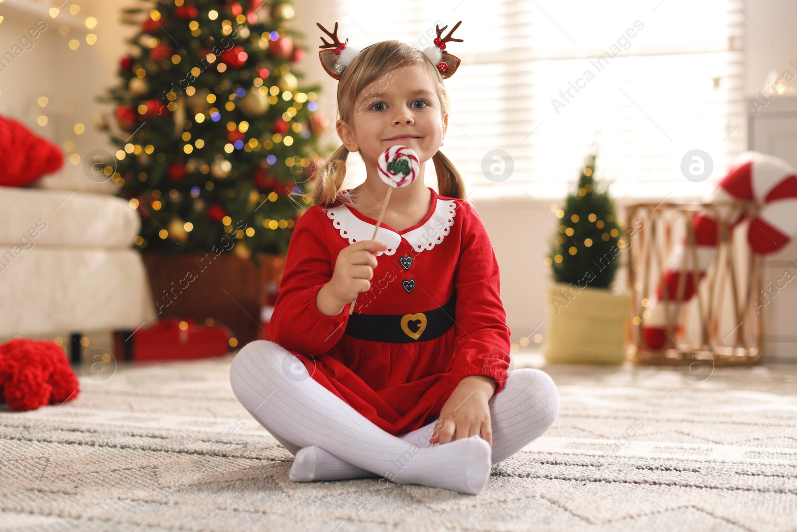 Photo of Little girl in Christmas costume with lollipop at home