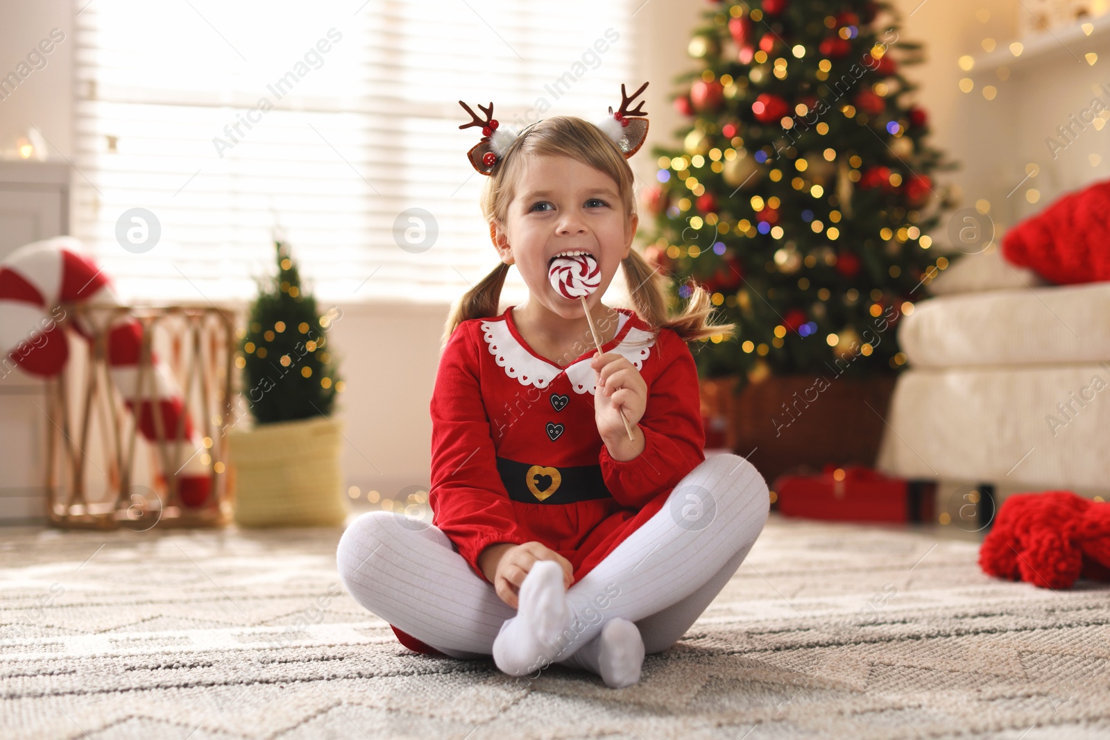 Photo of Little girl in Christmas costume with lollipop at home