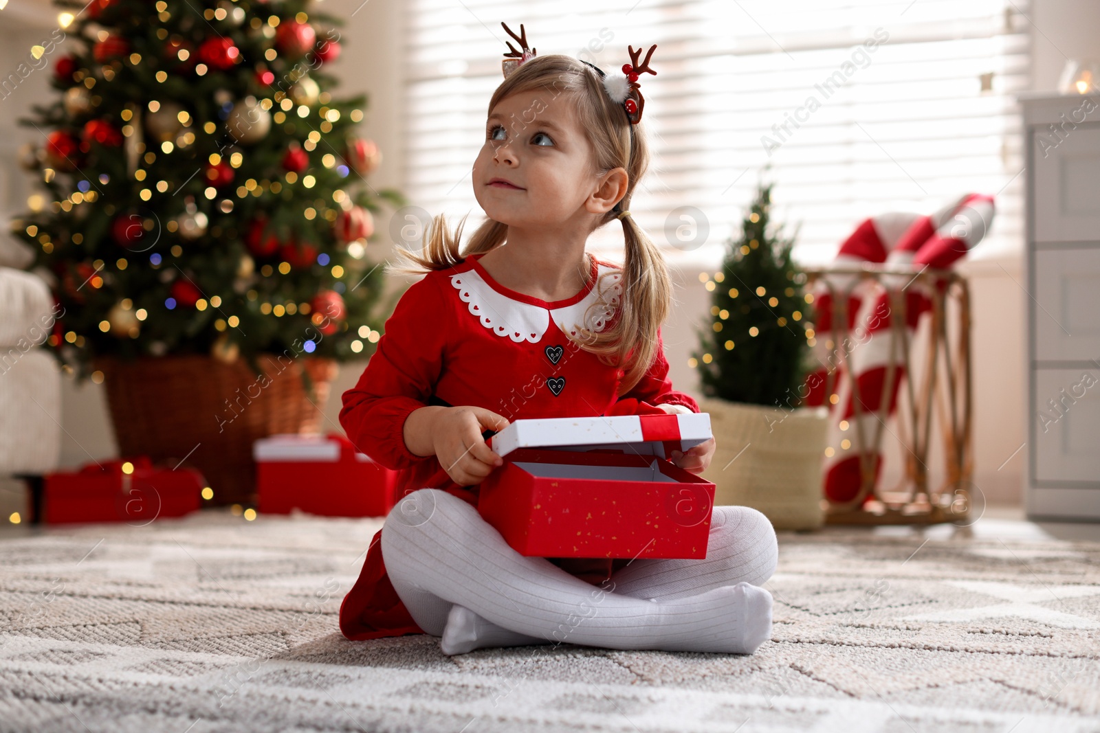 Photo of Little girl in Christmas costume with gift box at home