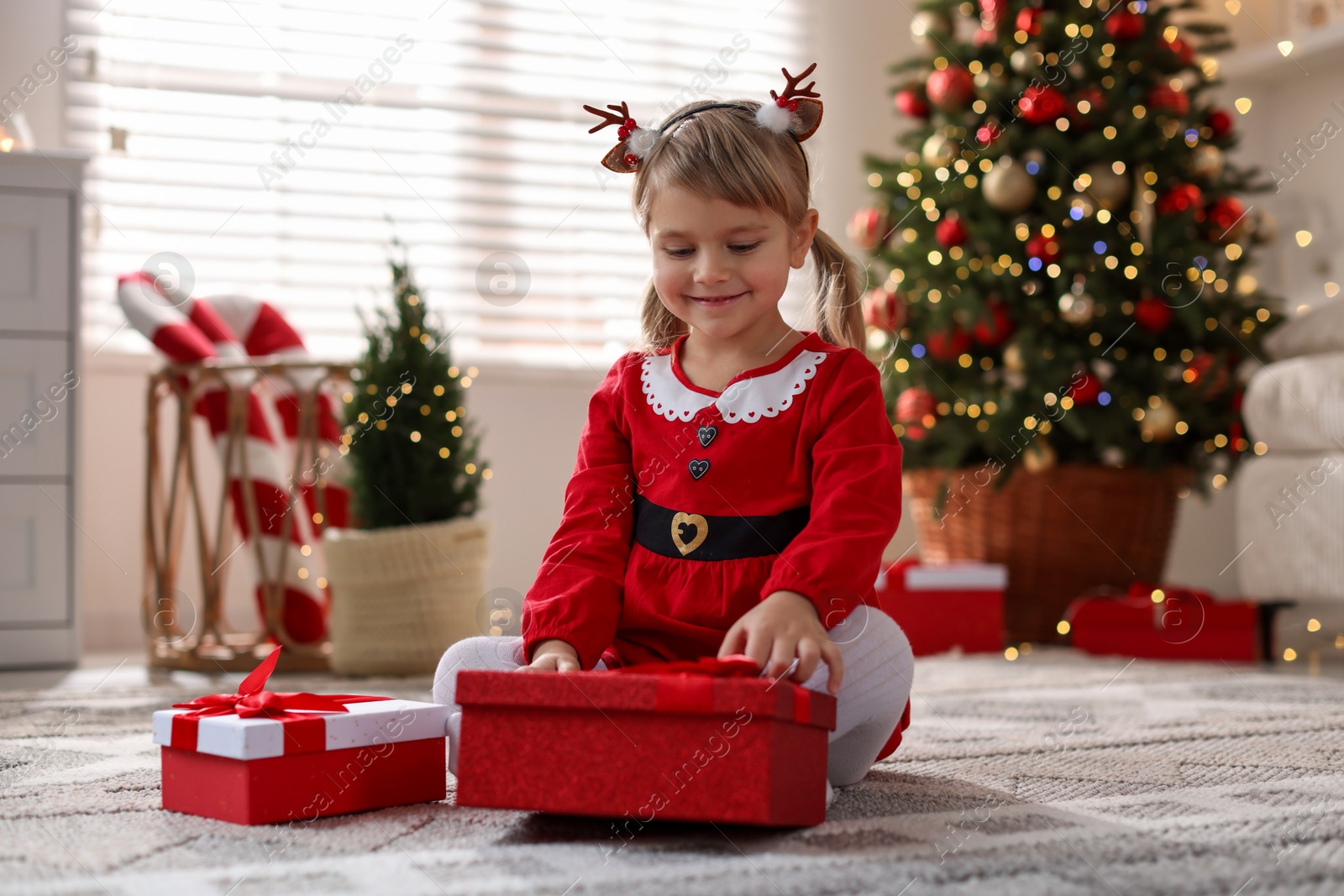 Photo of Little girl in Christmas costume with gift boxes at home