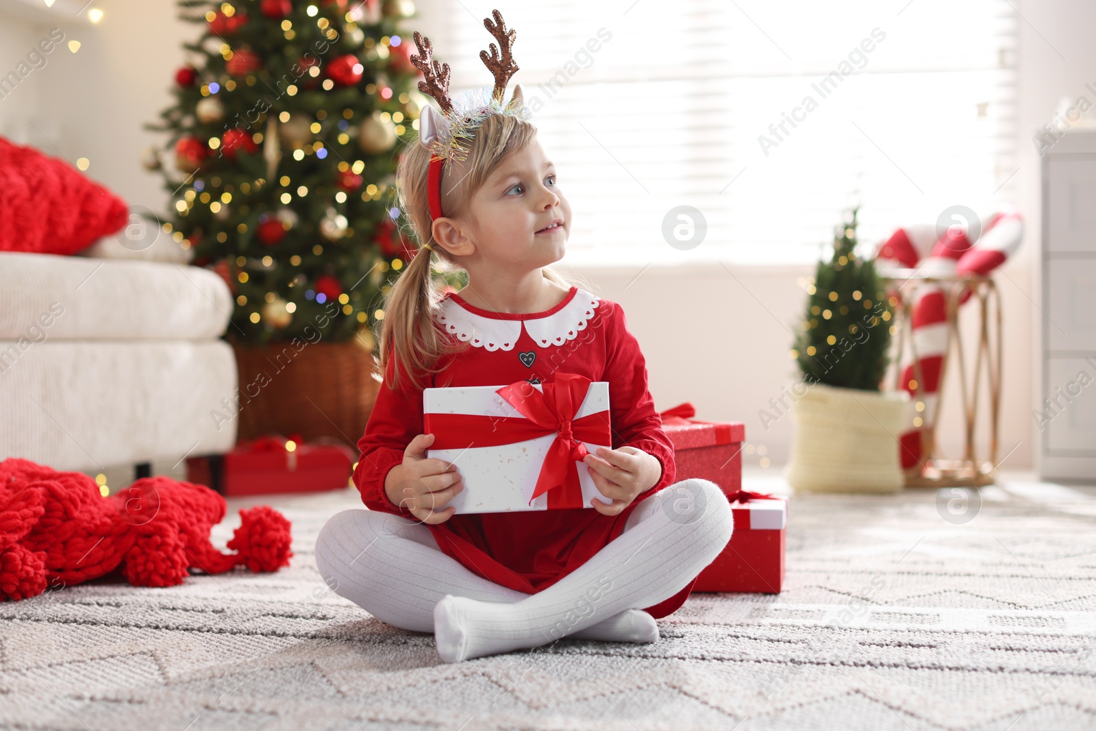 Photo of Little girl in Christmas costume with gift boxes at home