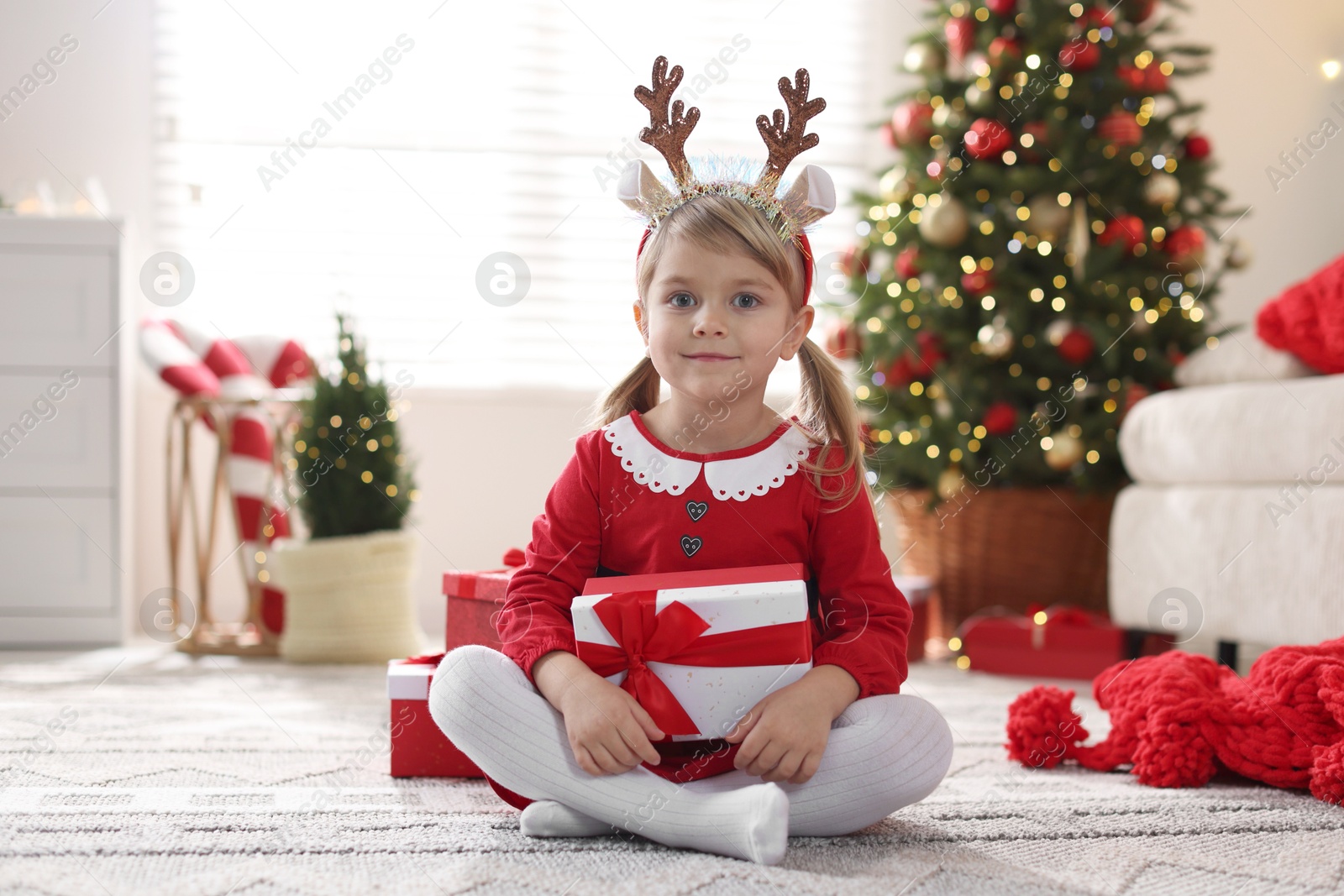 Photo of Little girl in Christmas costume with gift boxes at home