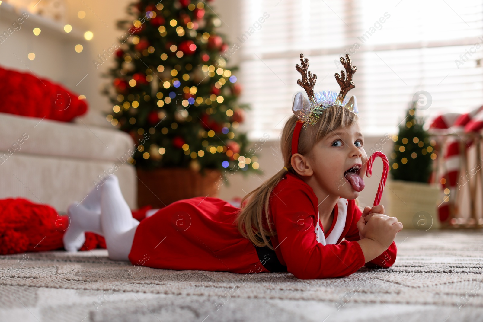 Photo of Little girl in Christmas costume with candy cane lying on floor at home