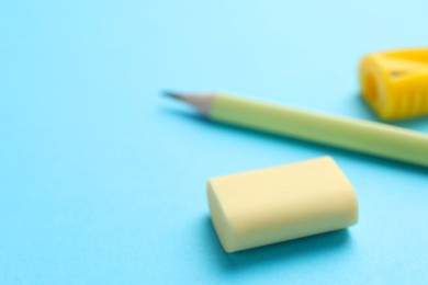 Photo of Eraser, pencil and sharpener on light blue background, selective focus. Space for text