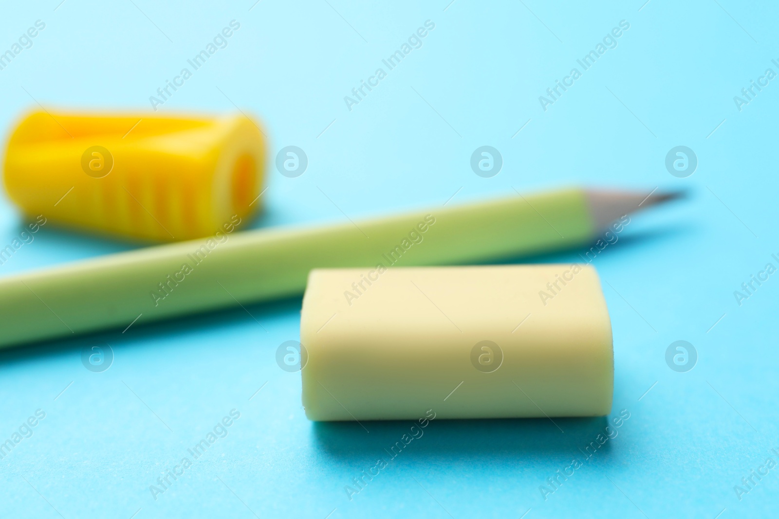 Photo of Eraser, pencil and sharpener on light blue background, selective focus