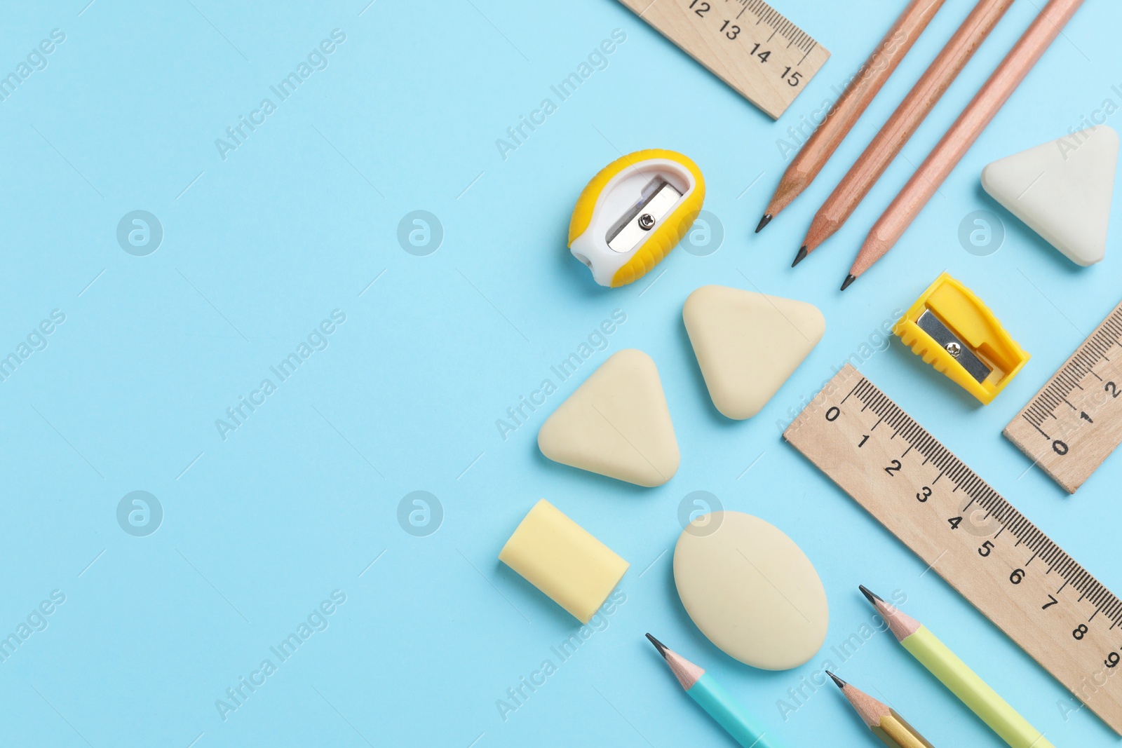 Photo of Erasers and other stationery on light blue background, flat lay. Space for text