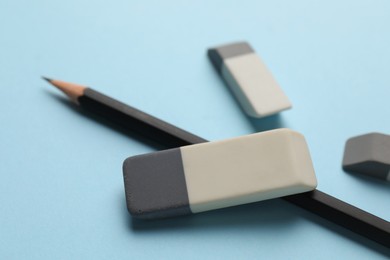 Photo of Erasers and pencil on light blue background, closeup