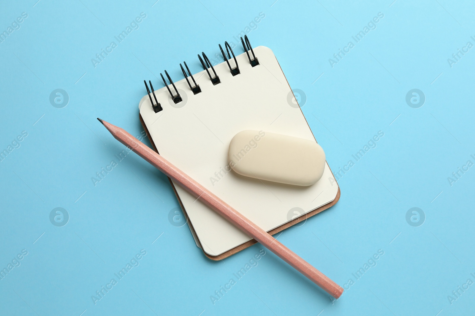 Photo of Eraser, pencil and notepad on light blue background, top view