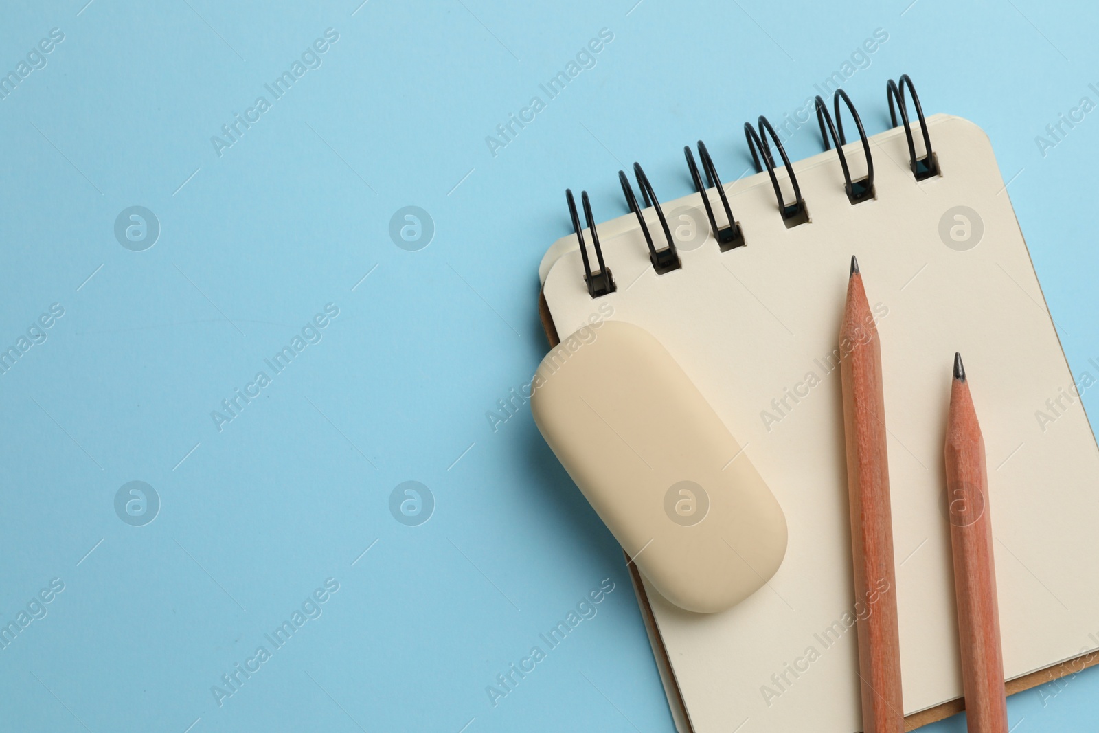 Photo of Eraser, pencils and notepad on light blue background, top view. Space for text