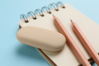 Photo of Eraser, pencils and notepad on light blue background, closeup