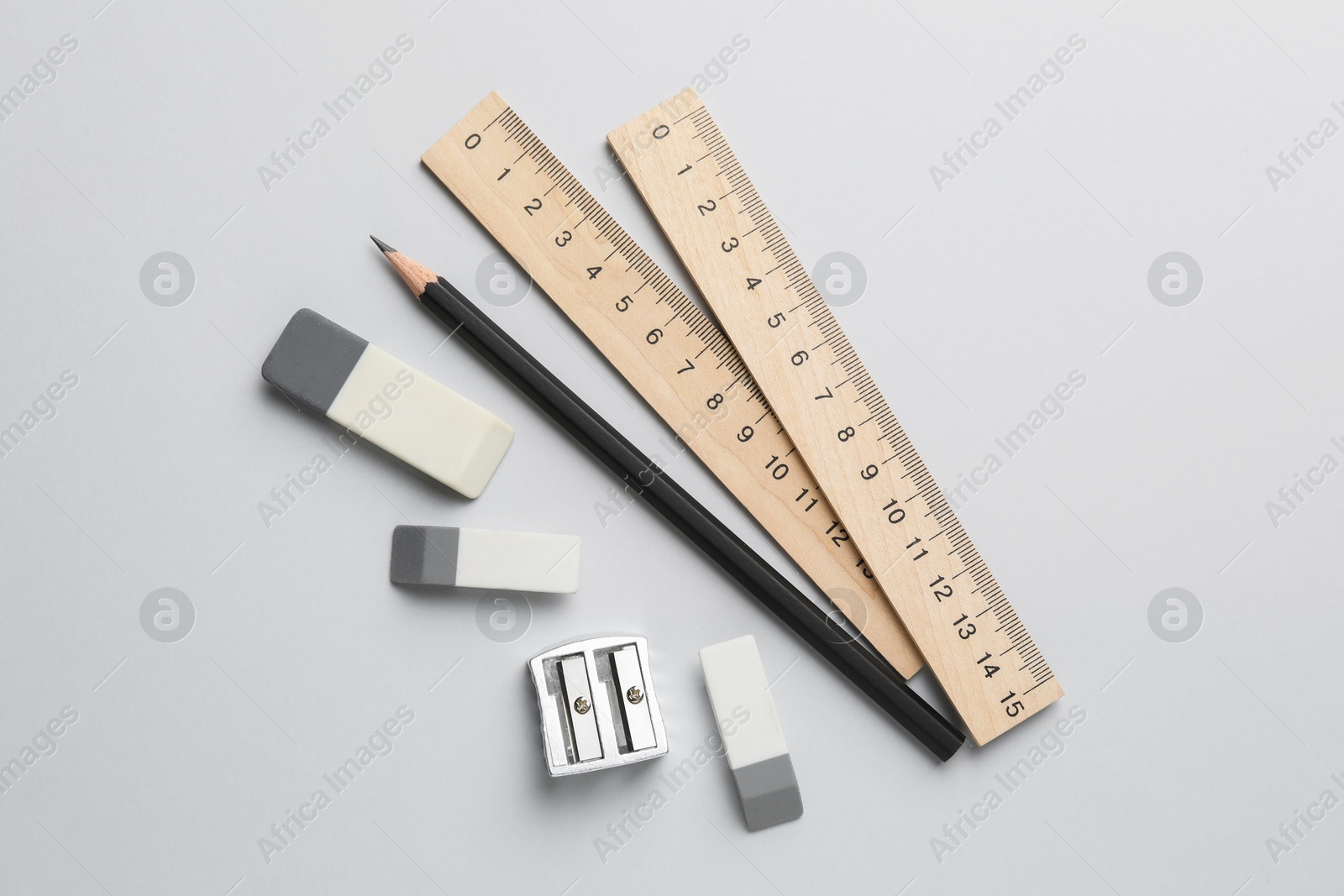 Photo of Erasers, pencil, sharpener and rulers on light background, top view