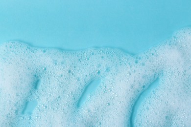 Photo of White fluffy foam on light blue background, top view. Space for text