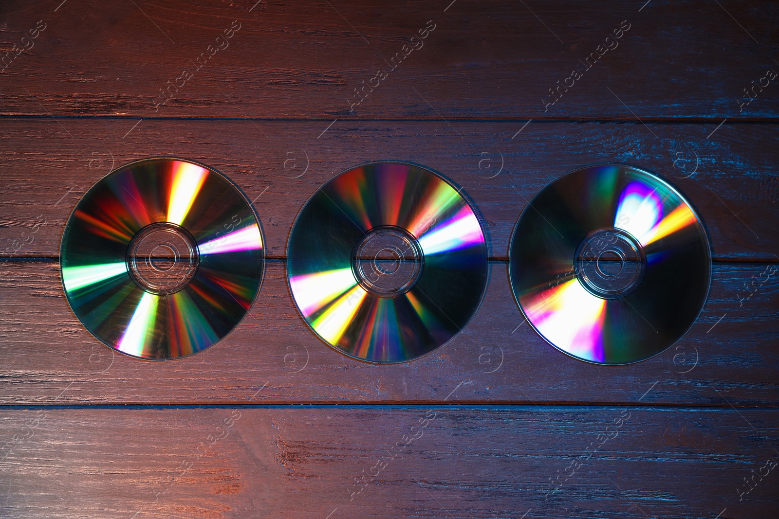 Photo of Shiny compact discs on wooden background, flat lay