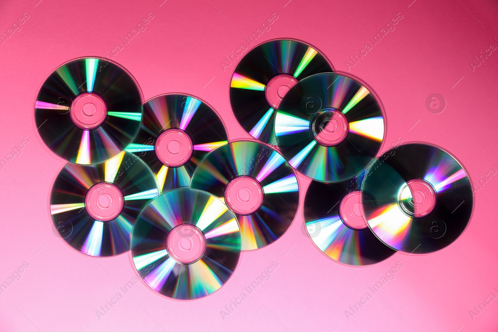 Photo of Many shiny compact discs on pink background, flat lay