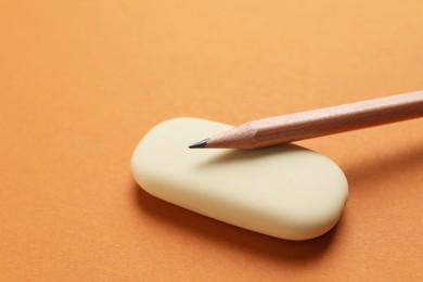 Photo of Eraser and pencil on orange background, closeup. Space for text