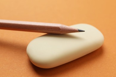 Photo of Eraser and pencil on orange background, closeup