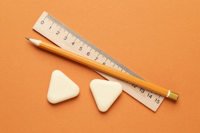 Photo of Erasers, ruler and pencil on orange background, flat lay