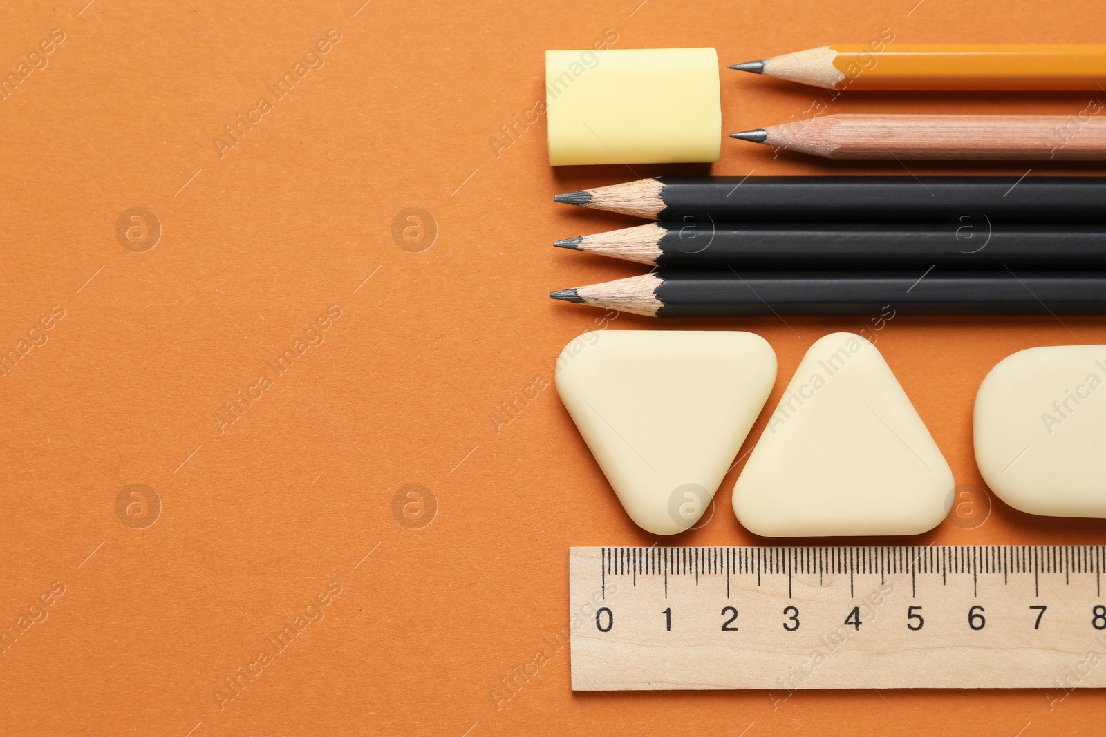 Photo of Erasers, ruler and pencils on orange background, flat lay. Space for text