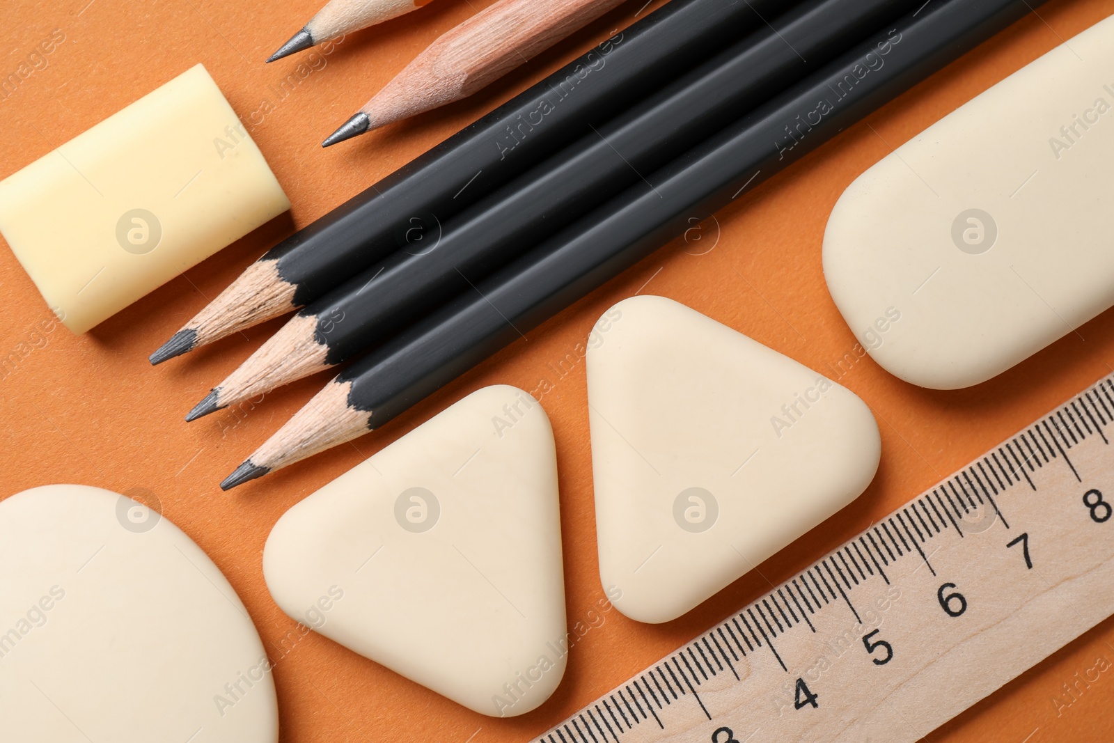 Photo of Erasers, ruler and pencils on orange background, flat lay