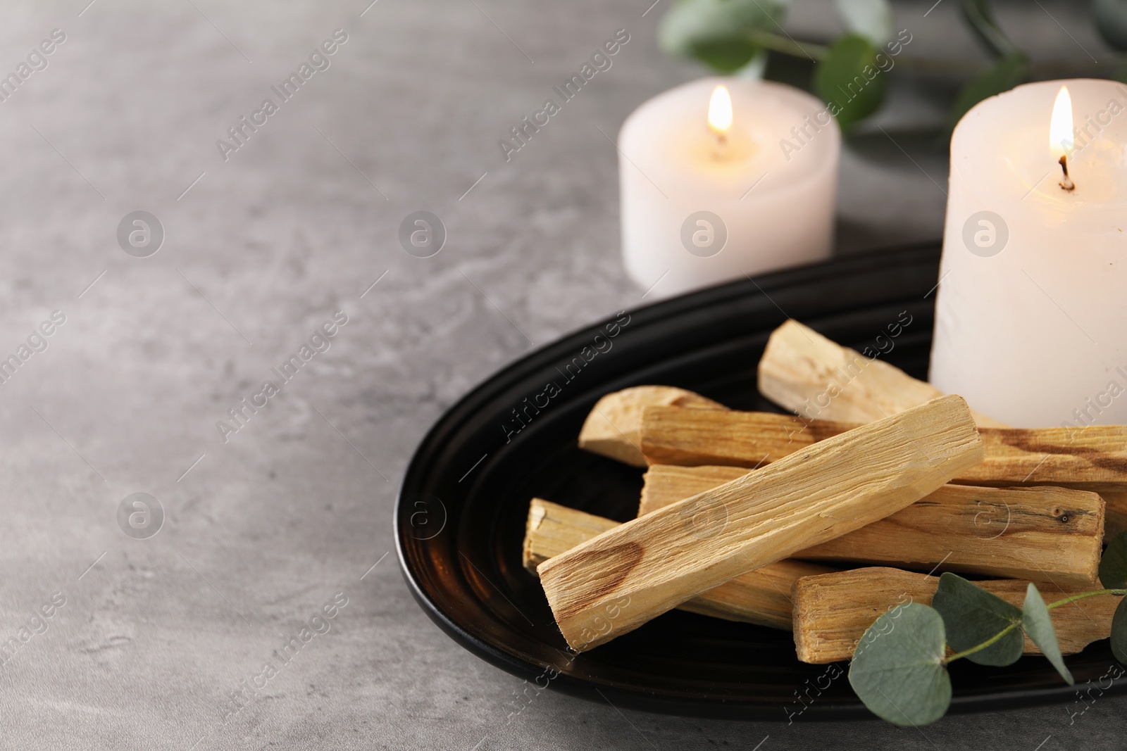 Photo of Palo santo sticks, eucalyptus branch and burning candles on grey table, closeup. Space for text