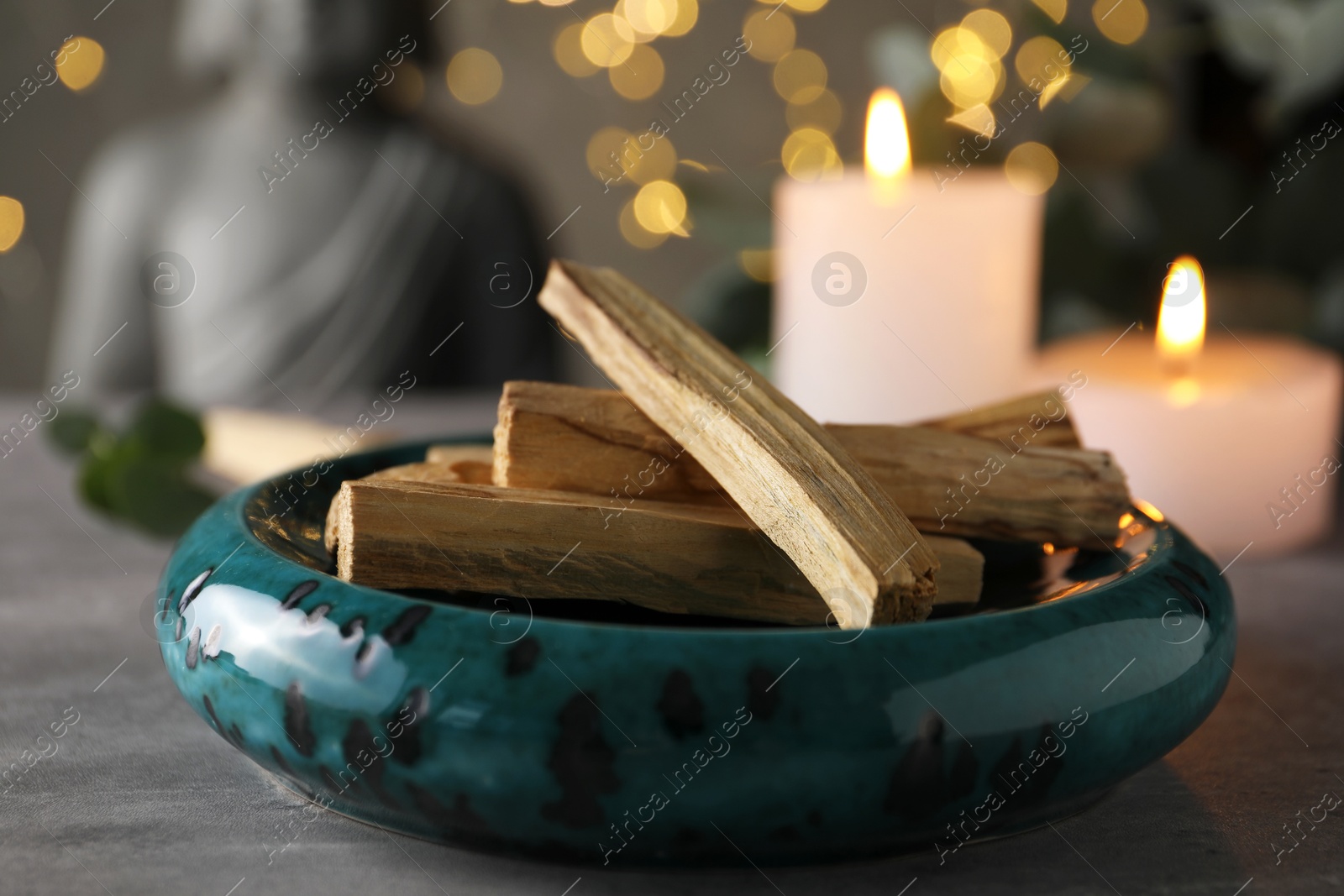 Photo of Palo santo sticks and burning candles on grey table, closeup