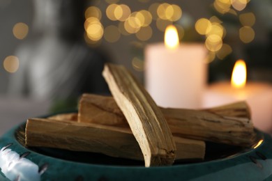 Photo of Palo santo sticks and burning candles on table, closeup