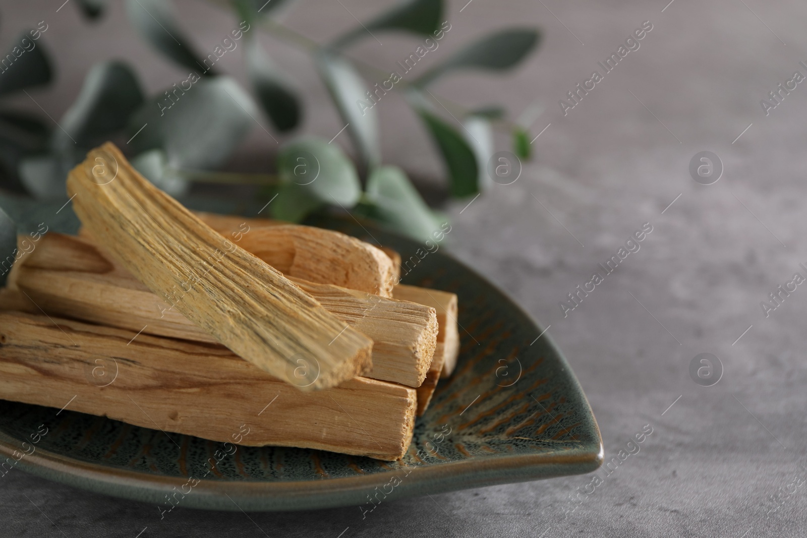 Photo of Palo santo sticks and eucalyptus leaves on grey table, closeup