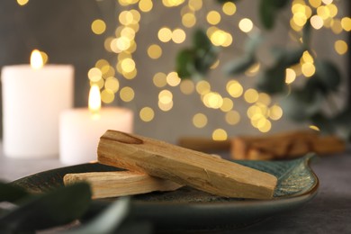 Photo of Palo santo sticks, eucalyptus leaves and burning candles on table, closeup