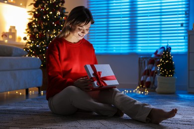 Photo of Happy woman with Christmas gift on floor at home