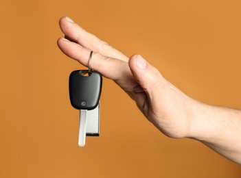 Photo of Man with car key and keychain on orange background, closeup