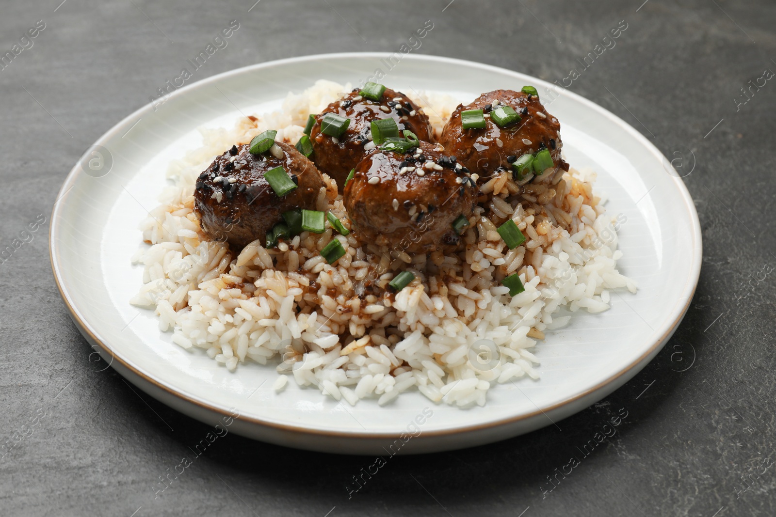 Photo of Delicious rice with meatballs, sauce and green onions on black table, closeup