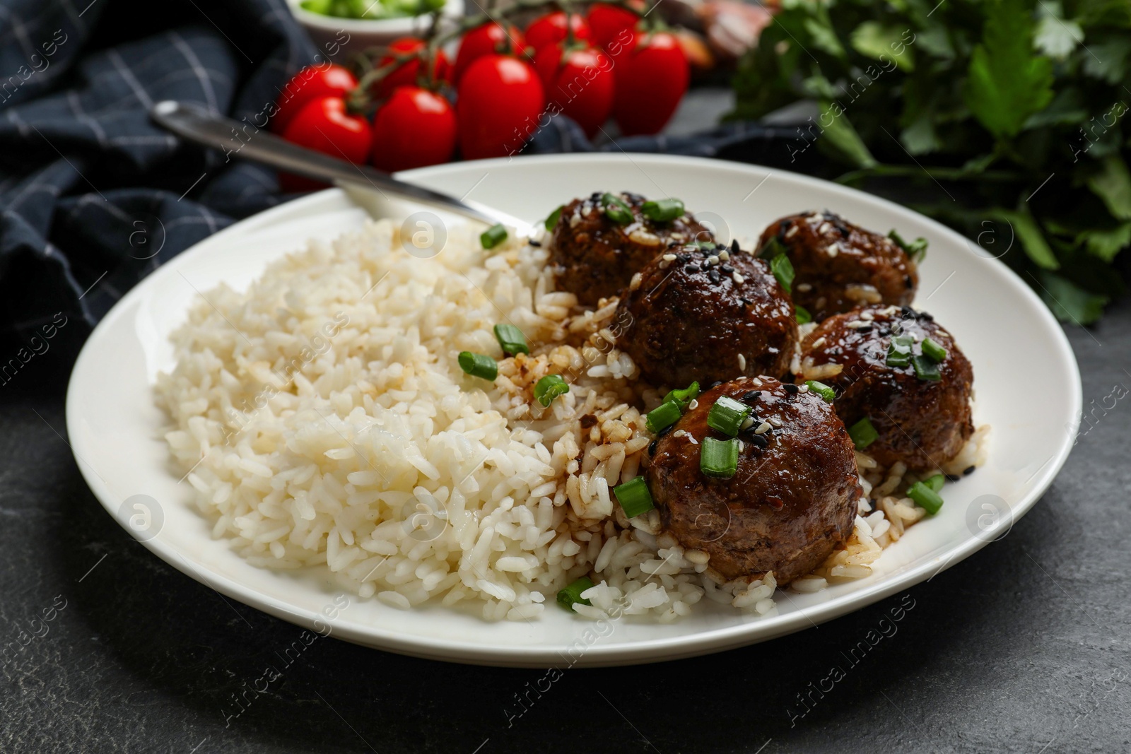 Photo of Delicious rice with meatballs, sauce and green onions on black table, closeup