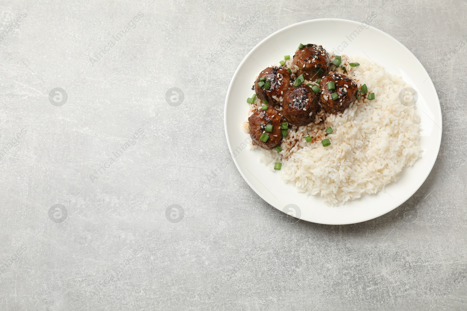 Photo of Delicious rice with meatballs, sauce and green onions on grey table, top view. Space for text