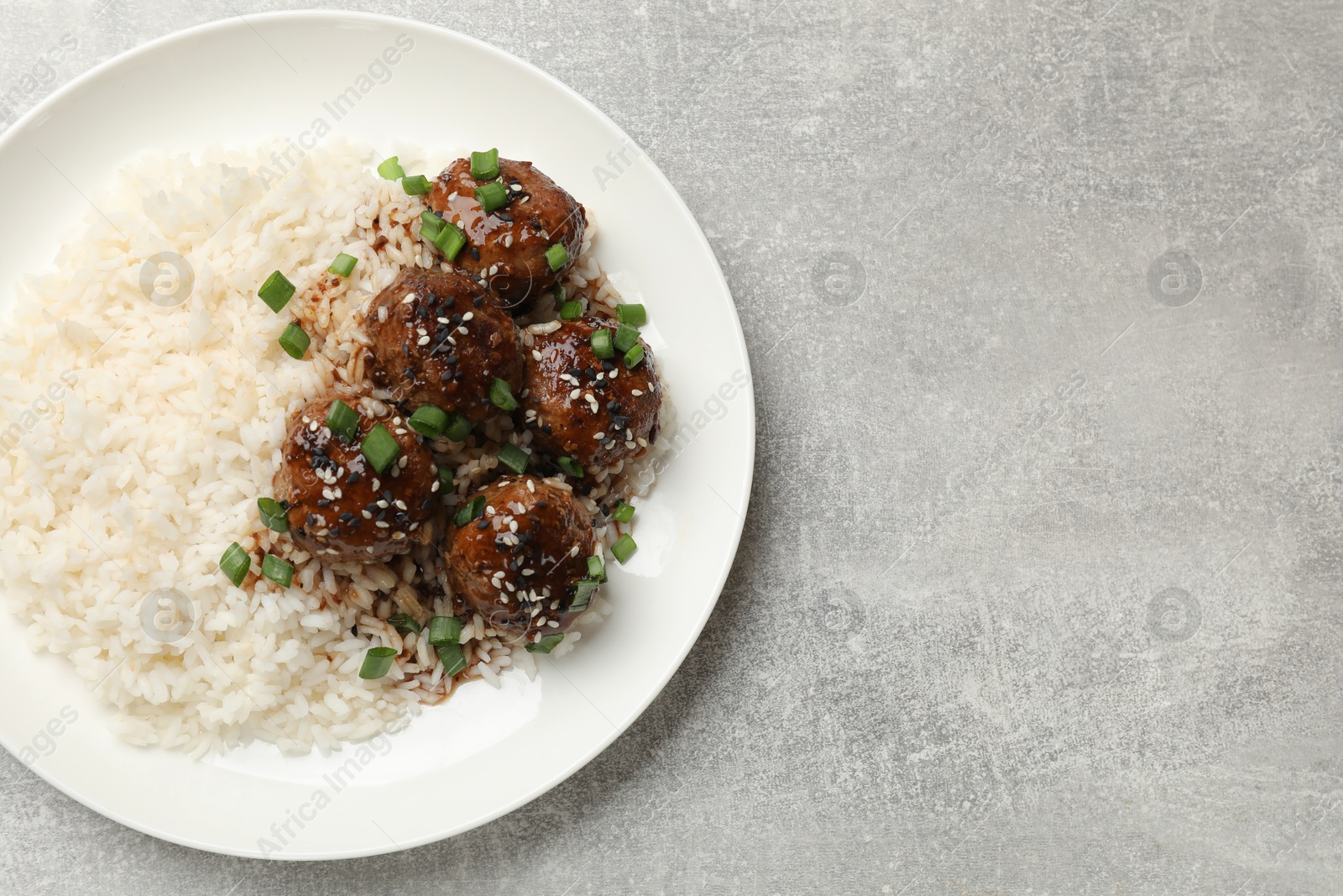 Photo of Delicious rice with meatballs, sauce and green onions on grey table, top view. Space for text