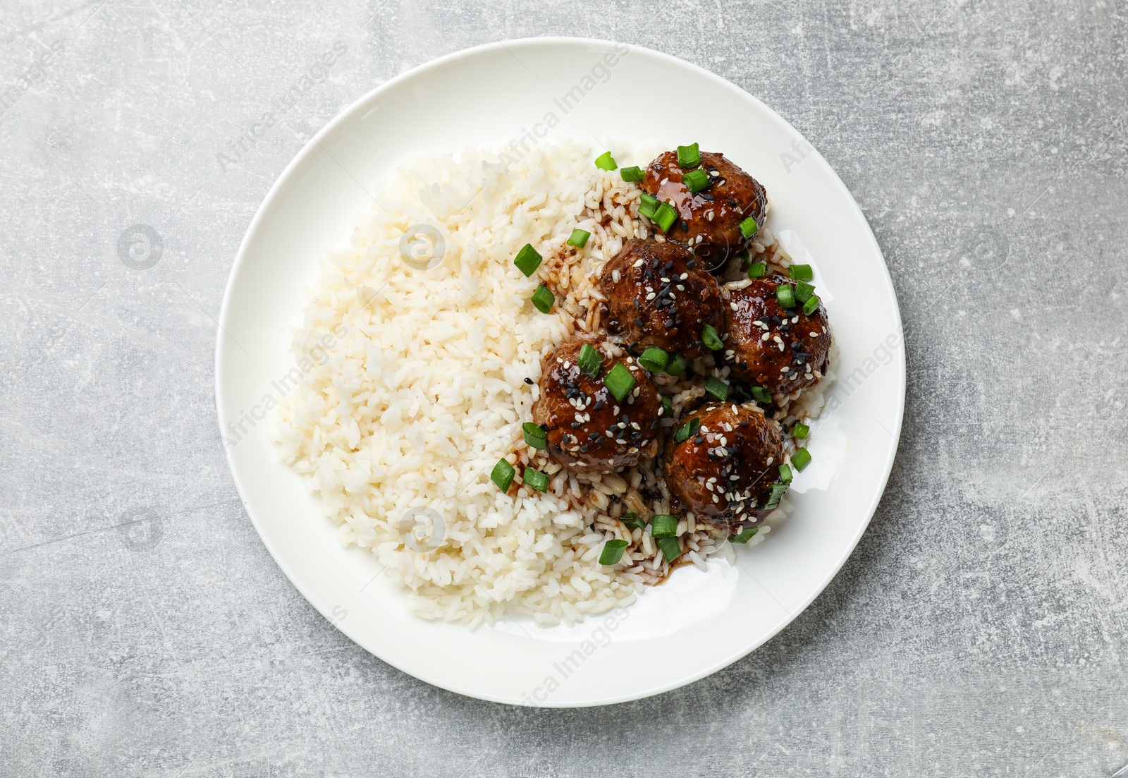 Photo of Delicious rice with meatballs, sauce and green onions on grey table, top view