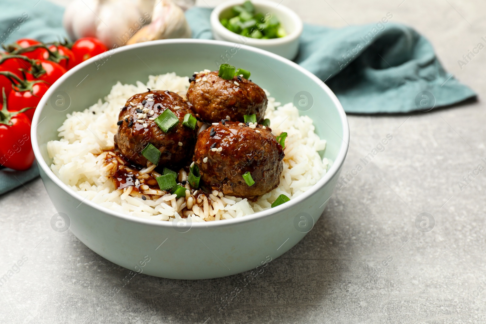 Photo of Delicious rice with meatballs, sauce and green onions on grey table, closeup