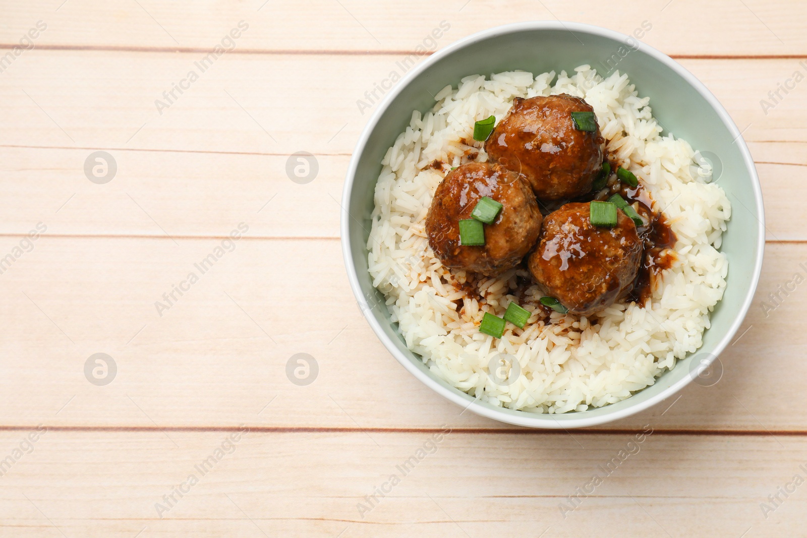 Photo of Delicious rice with meatballs, sauce and green onions in bowl on white wooden table, top view. Space for text