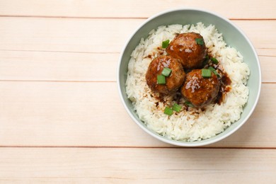 Photo of Delicious rice with meatballs, sauce and green onions in bowl on white wooden table, top view. Space for text