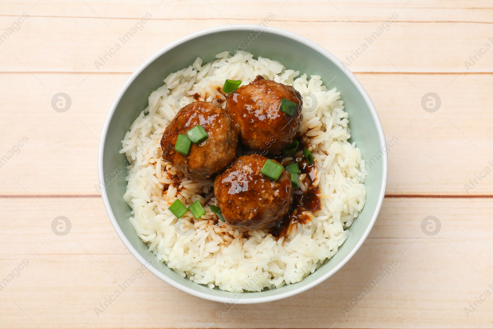 Photo of Delicious rice with meatballs, sauce and green onions in bowl on white wooden table, top view