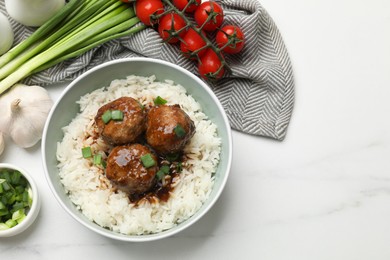 Photo of Delicious rice with meatballs, sauce and green onions on white marble table, flat lay