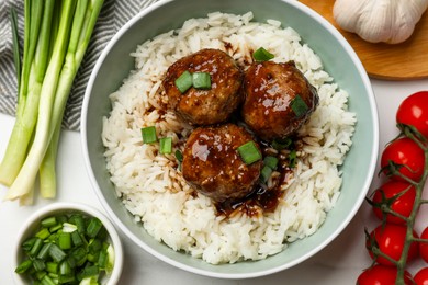 Photo of Delicious rice with meatballs, sauce and green onions on white table, flat lay