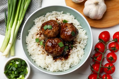 Photo of Delicious rice with meatballs, sauce and green onions on white table, flat lay